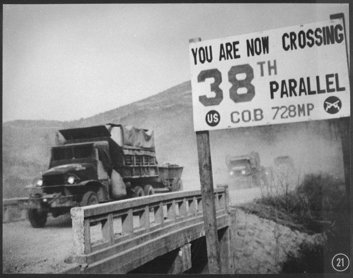 Camions militaires franchissant le 38e parallèle en Corée, en 1950, devant le panneau planté par l'armée américaine.