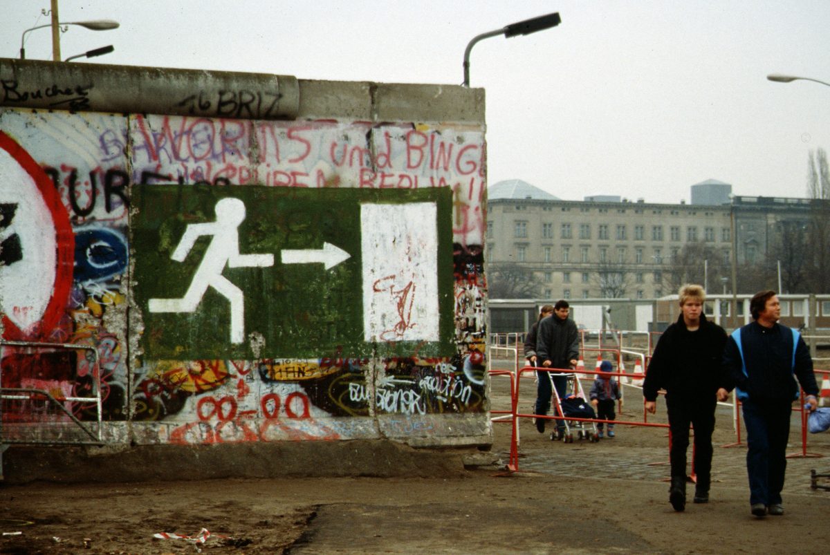 Berlin, novembre 1989 : des passants traversent une brèche ouverte dans le mur, côté ouest couvert de graffitis.
