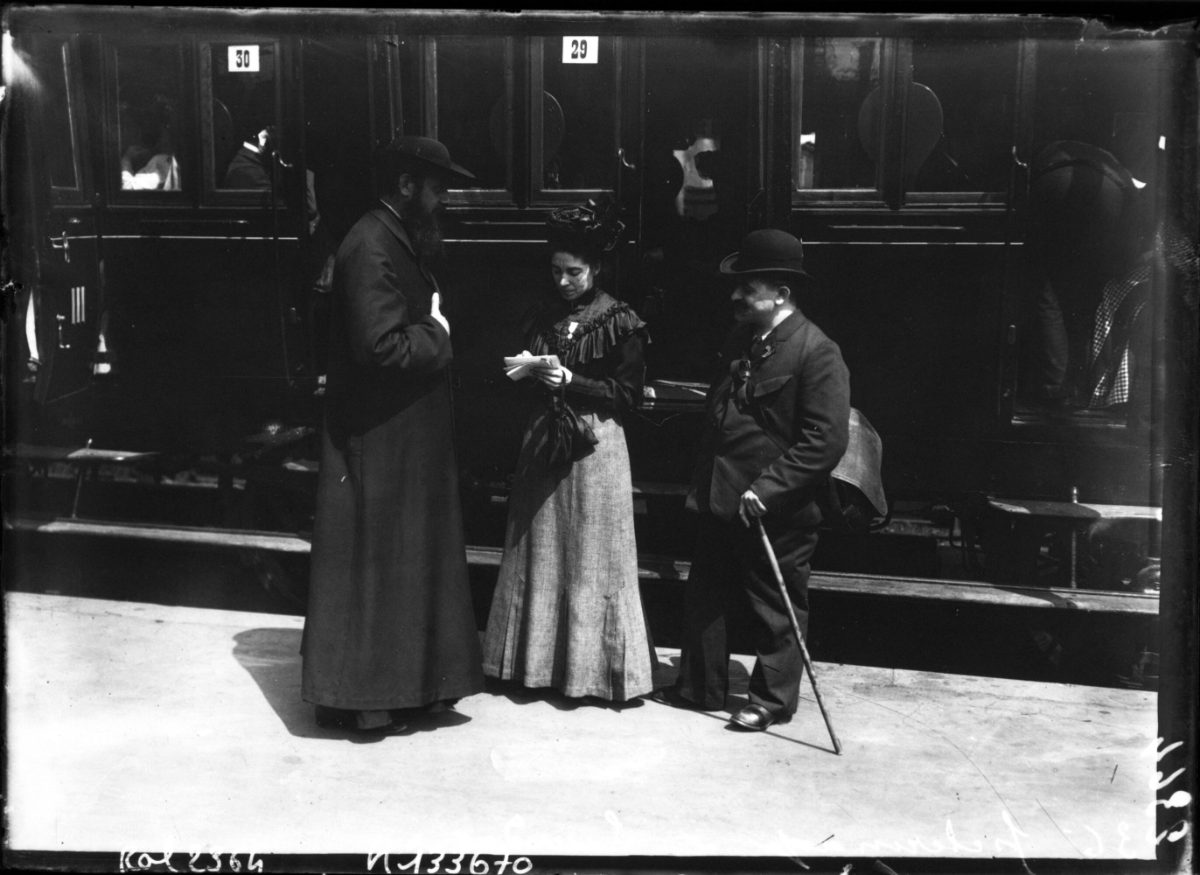 Gare d'Austerlitz, 1908 : un prêtre et deux pèlerins devant le train du pèlerinage national de Lourdes.